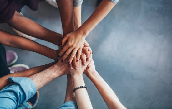 Image is taken from above and is of a group of people who have stacked their hands on top of each other. Disability advocacy communities. Inform online.