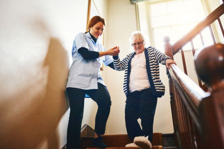 Woman helping lady down the stairs Disability Support Worker Assisting Lady down stairs