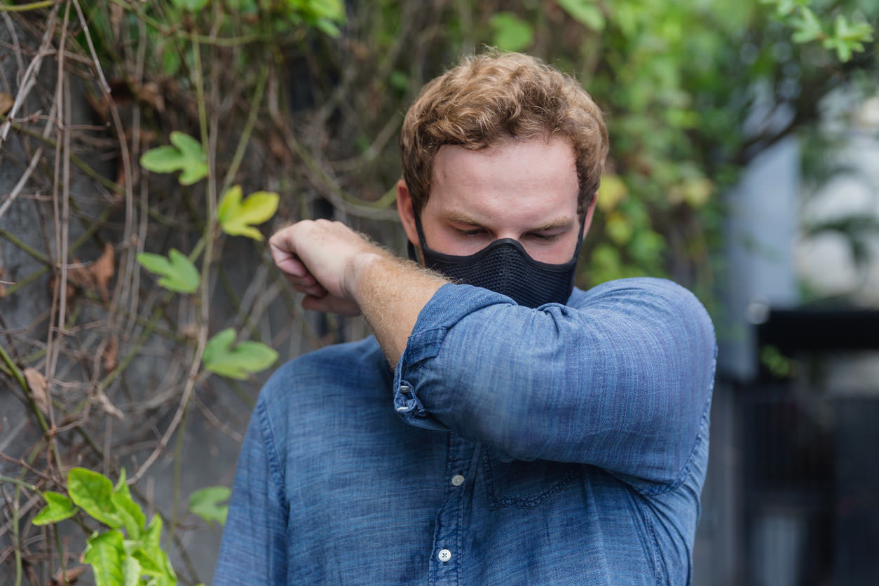 Man with a face mask sneezing into his elbow 