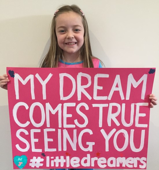 Little girl holding sign 'my dream comes true seeing you #littledreamers'