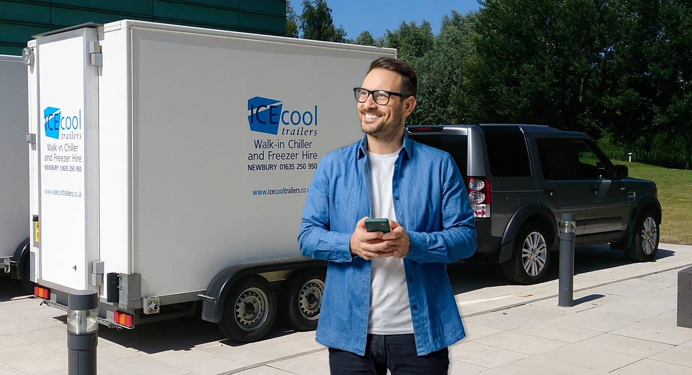 Person using a phone to book walk-in chiller trailer hire beside a towed trailer