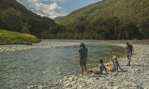 Four people standing and sitting alongside a river