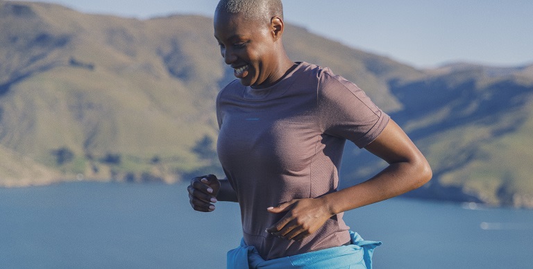 Woman jogging in front of a lake wearing pink icebreaker merino cool-lite sphere t-shirt