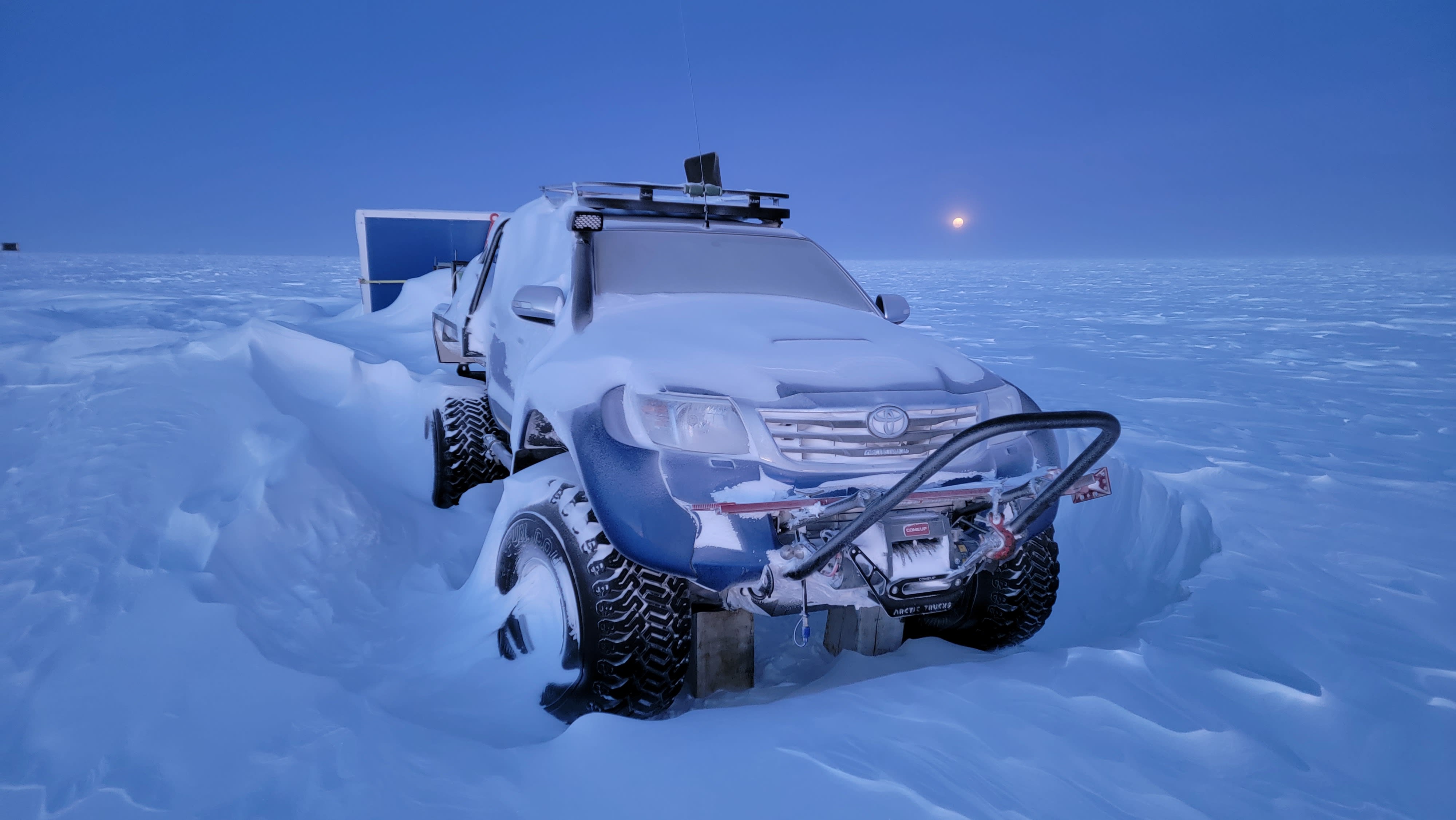 Front view of vehicle partially buried in snow at South Pole during twilight.