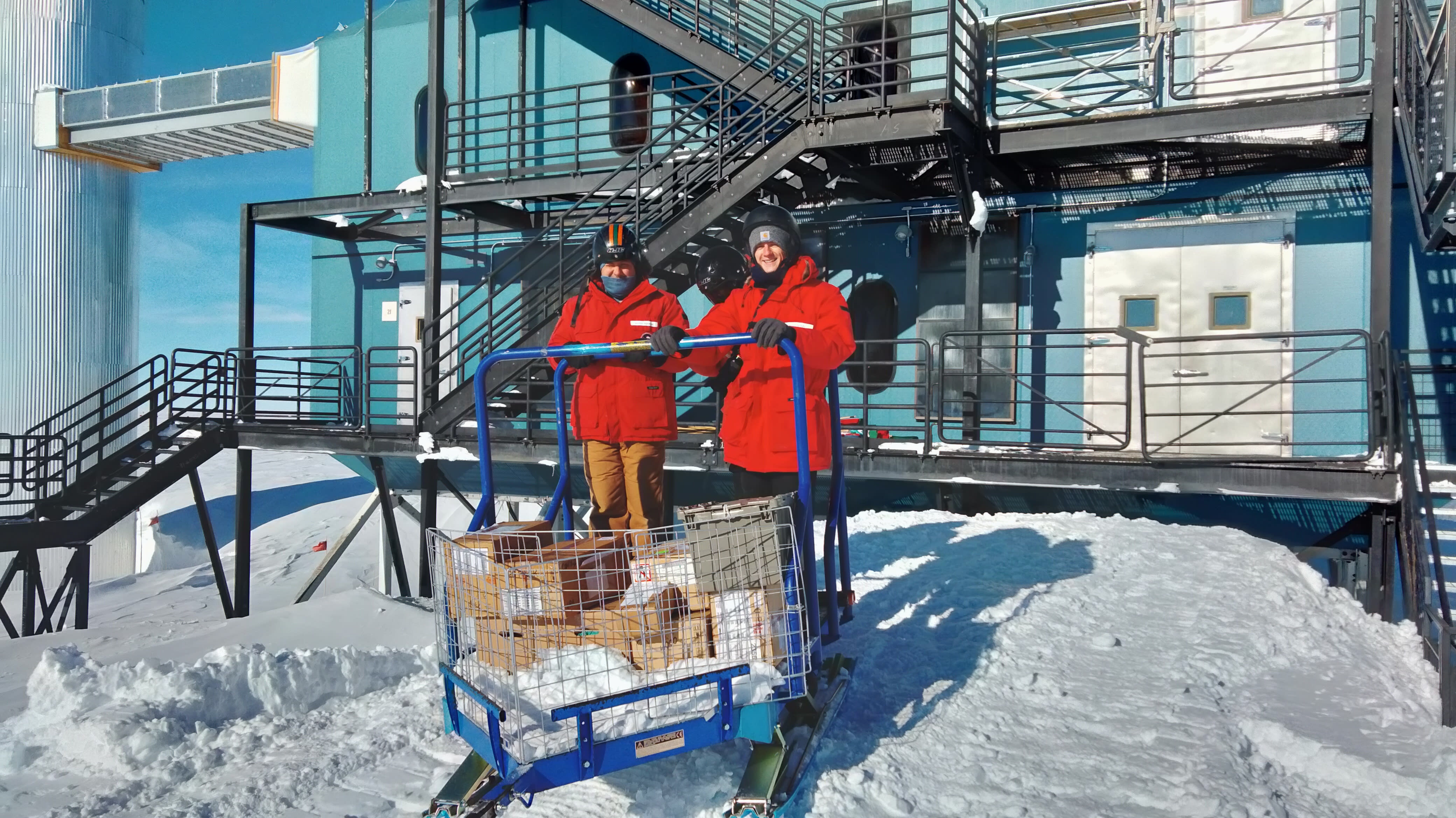 Two winterovers with a sled of cargo in front of the IceCube Lab.