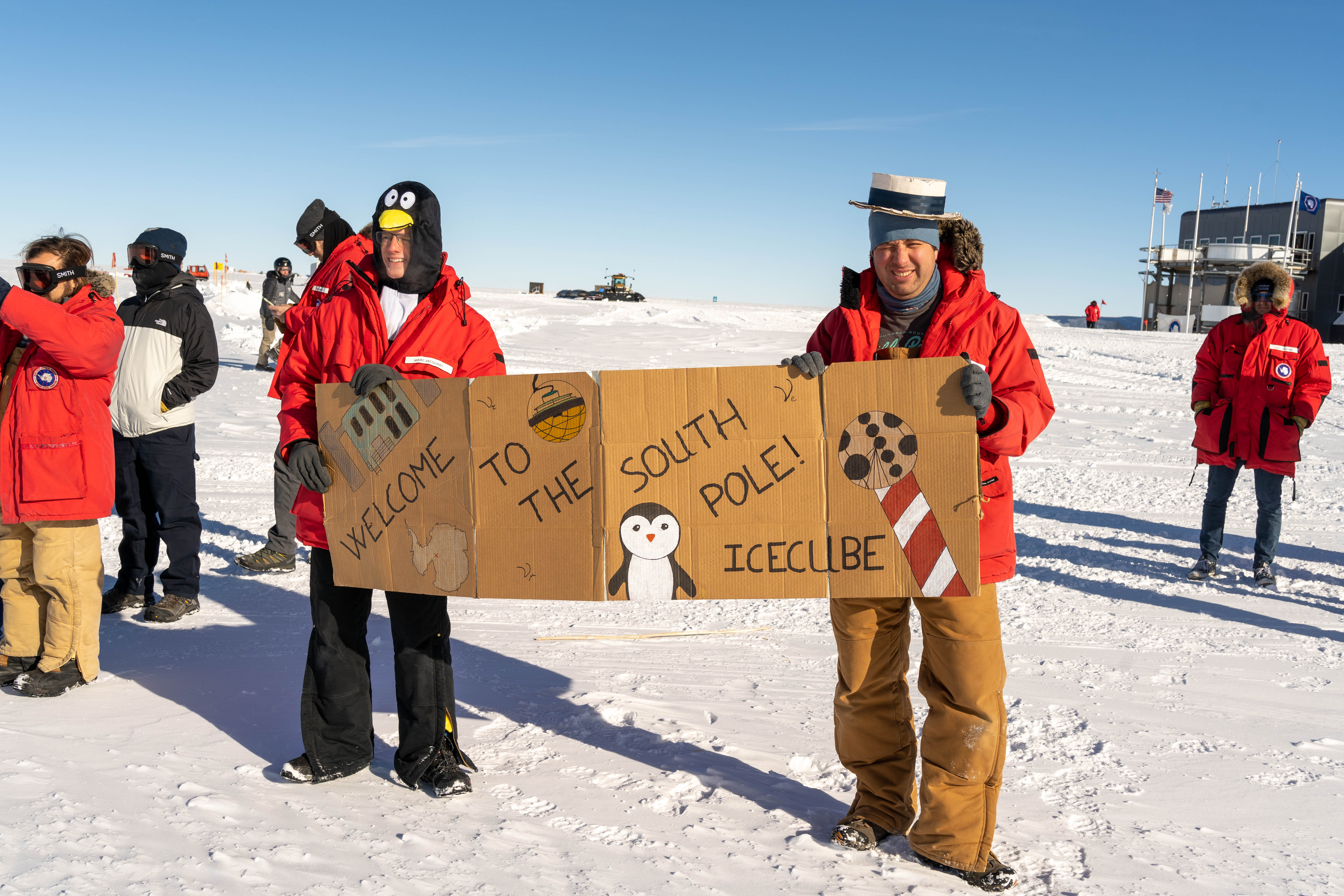 Two winterovers outside in costume holding a cardboard welcome sign.