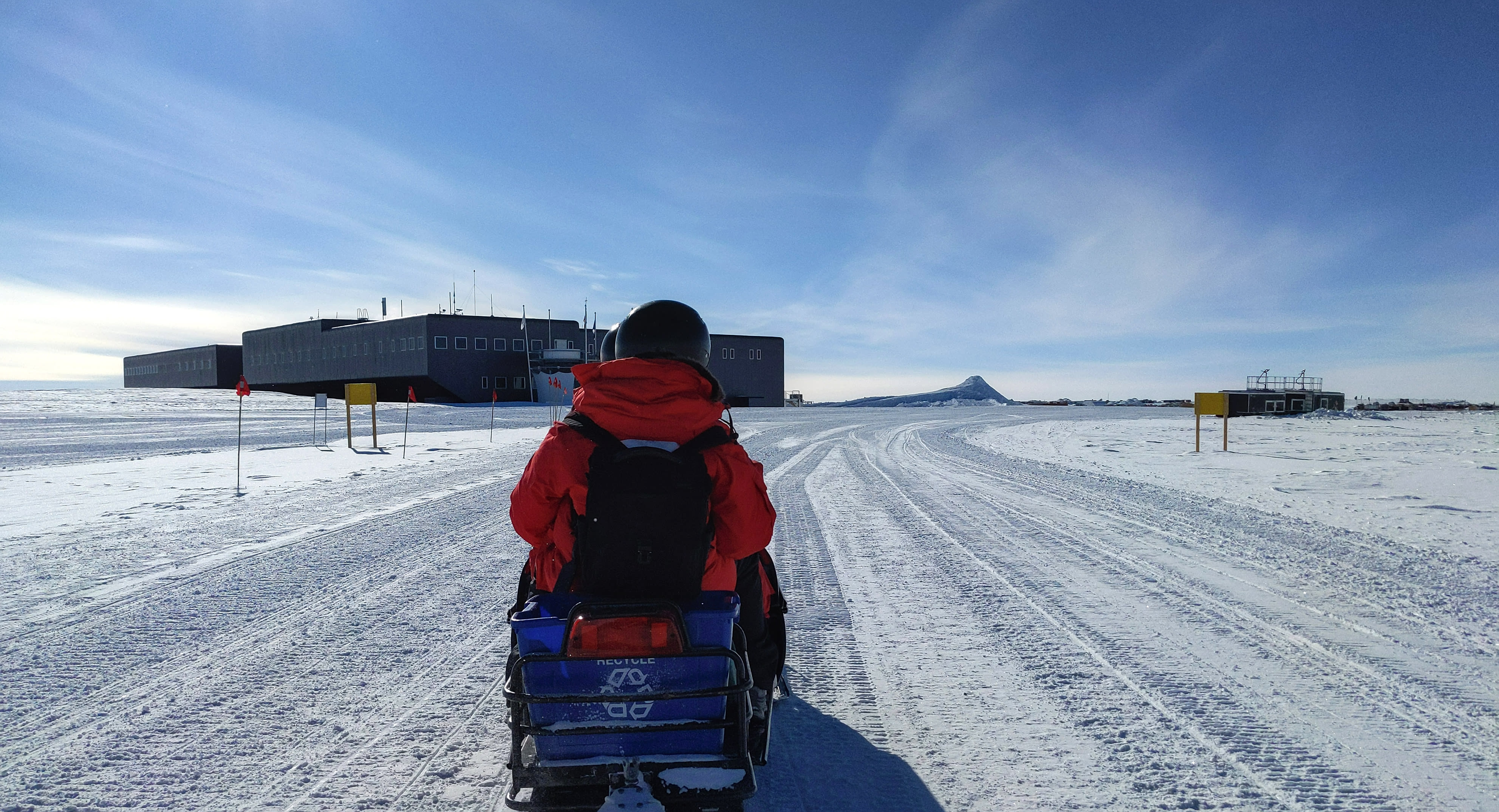 Person in red parka seen from behind on snowmobile headed toward station.