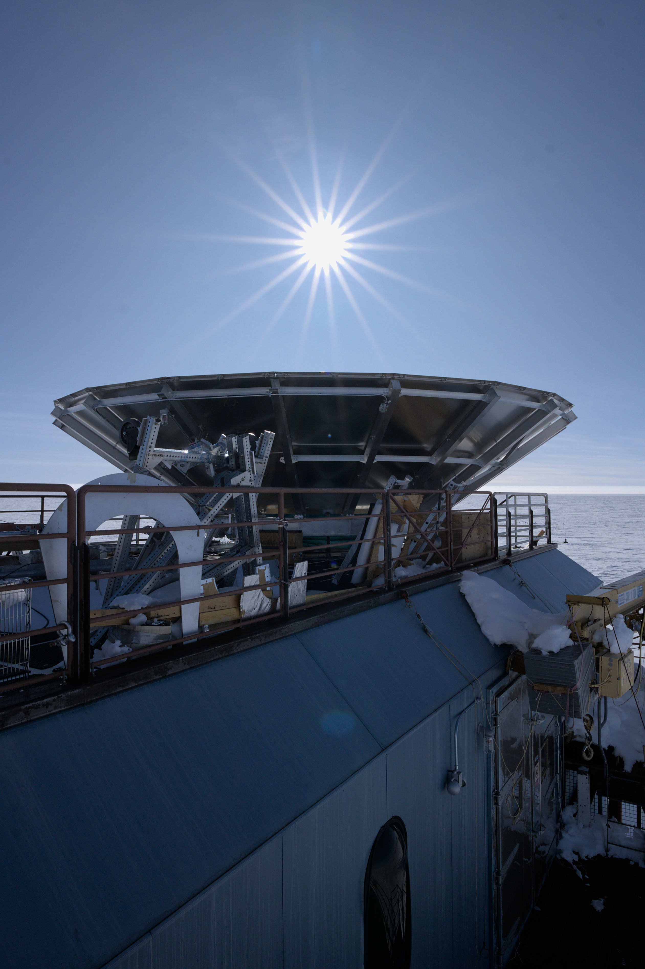 Top of BICEP telescope in foreground, bright starburst sun in sky overhead.