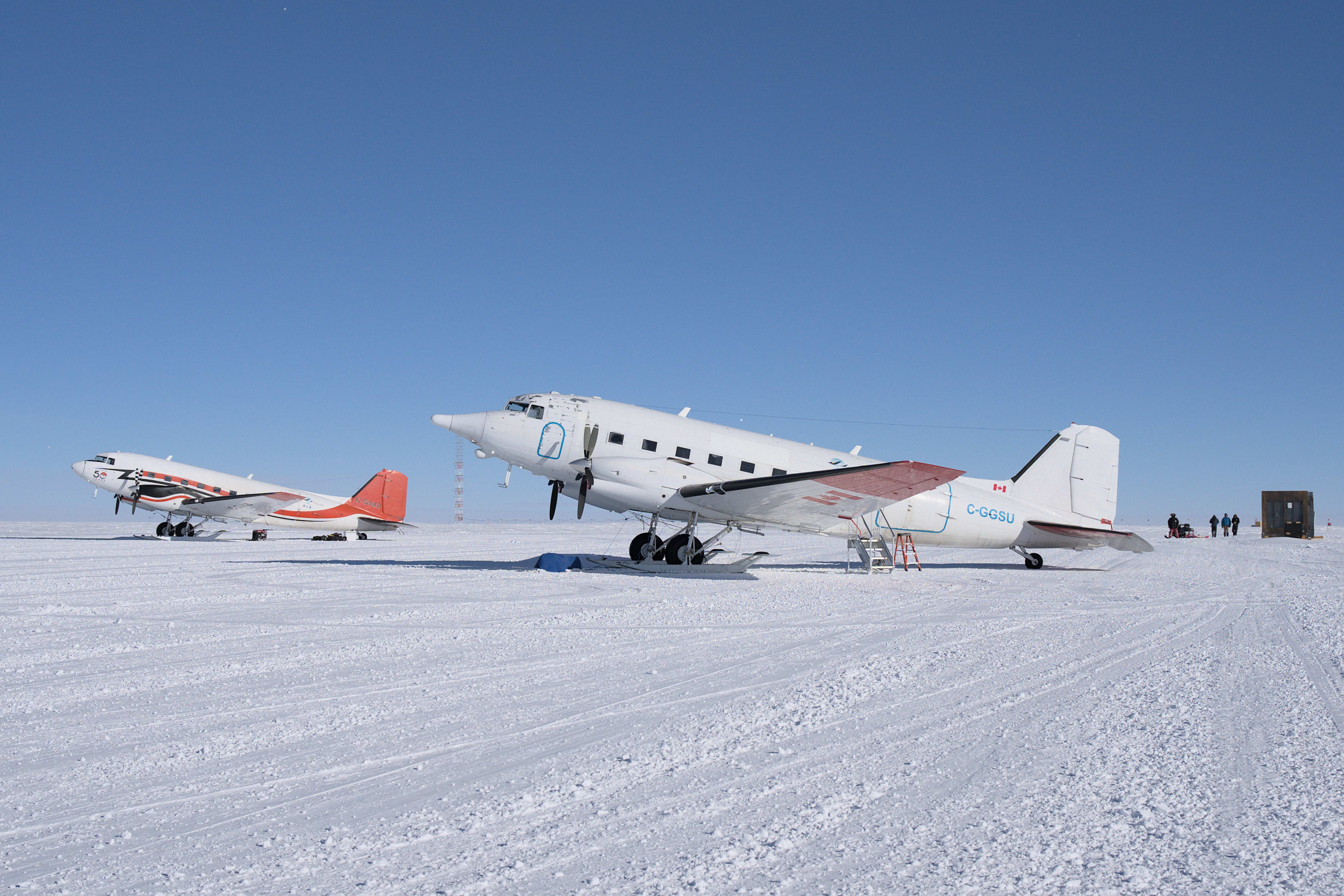 Side view of two small aircraft parked at the South Pole under clear blue sky.