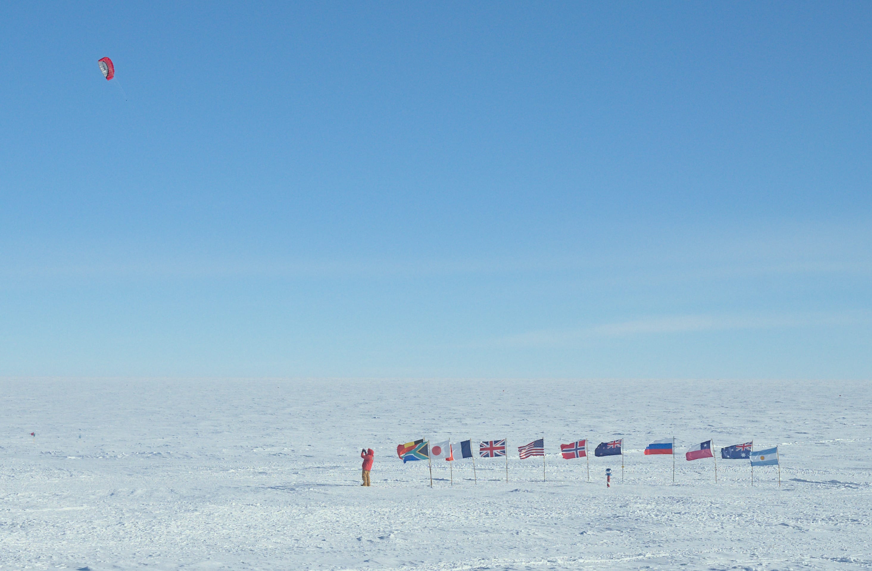 Person in red parka at the ceremonial Pole flying a kite high in the air.