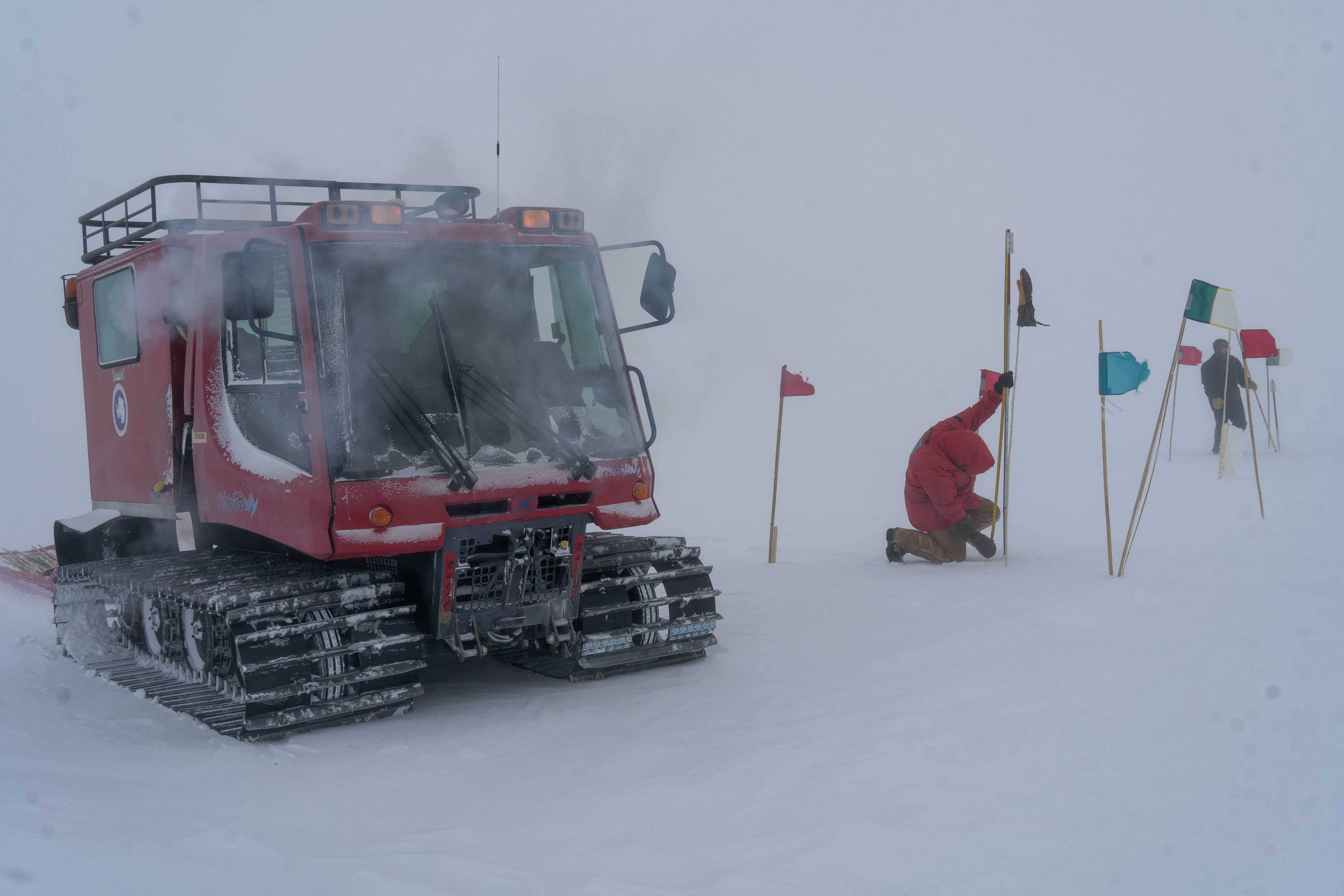 Two winterovers taking snow depth measurements outside at the Southh Pole with low visibility.