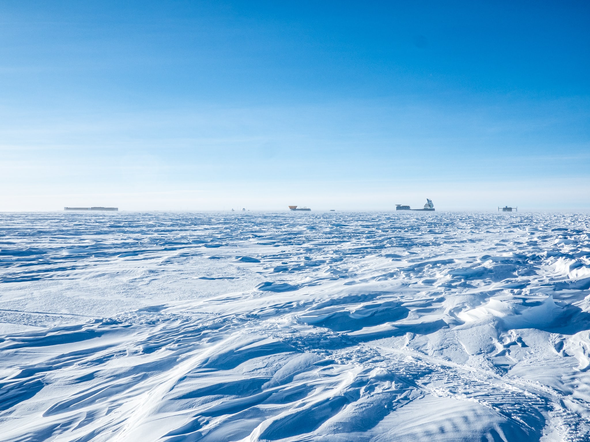 Clear blue skies, tiny South Pole buildings of the Dark Sector on the horizon.