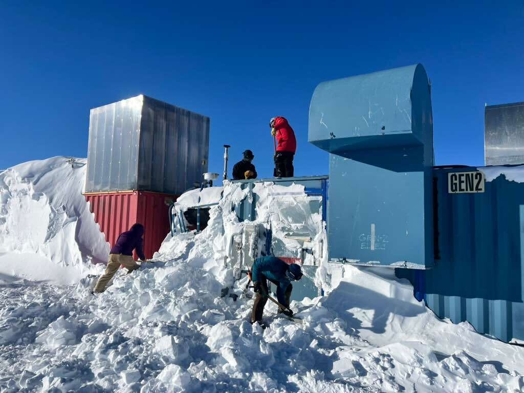 A group of people shoveling snow around buildings.