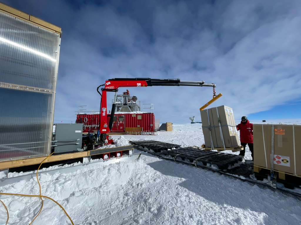 Crates getting moved and positioned on a sled by a small crane.
