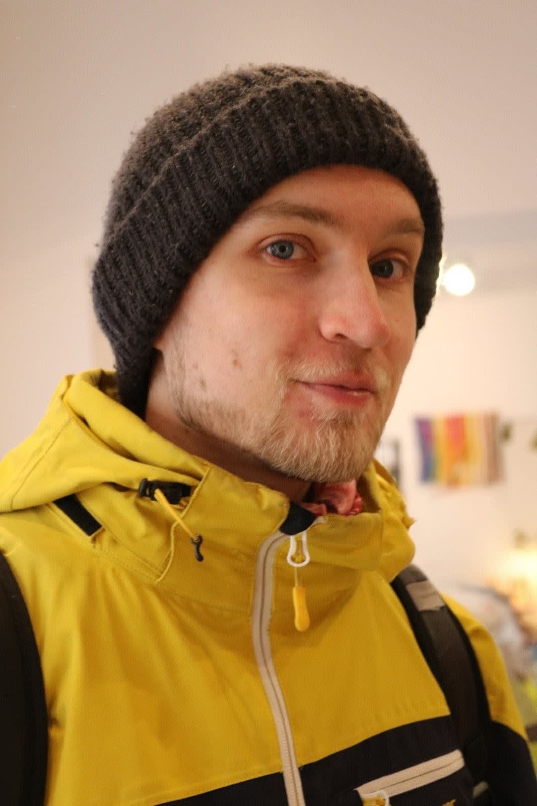 A man with a beanie and yellow jacket posing for a photo.