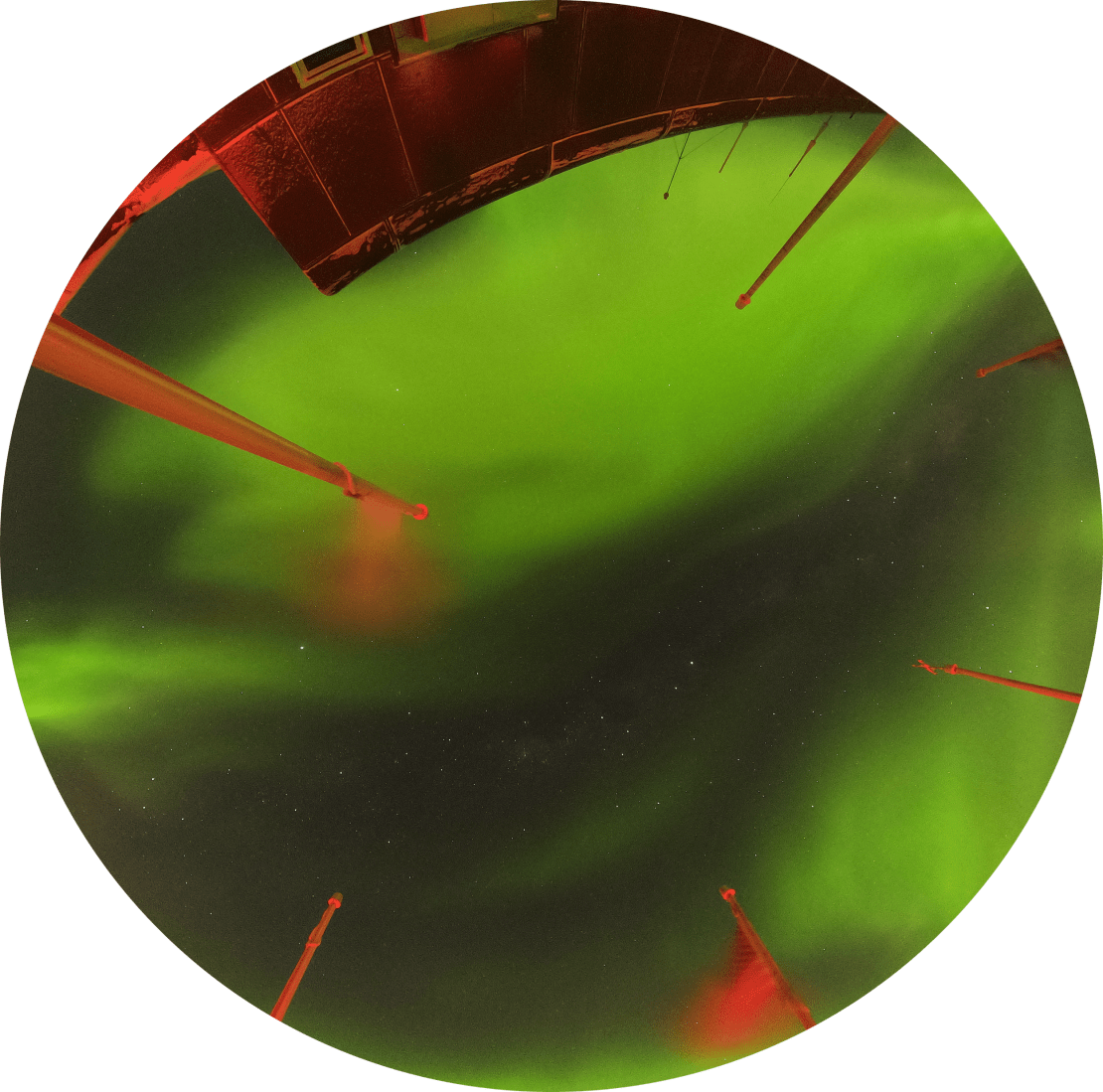 Fish-eye view looking up into the sky at a swirl of bright green auroras from the South Pole station’s observation deck.