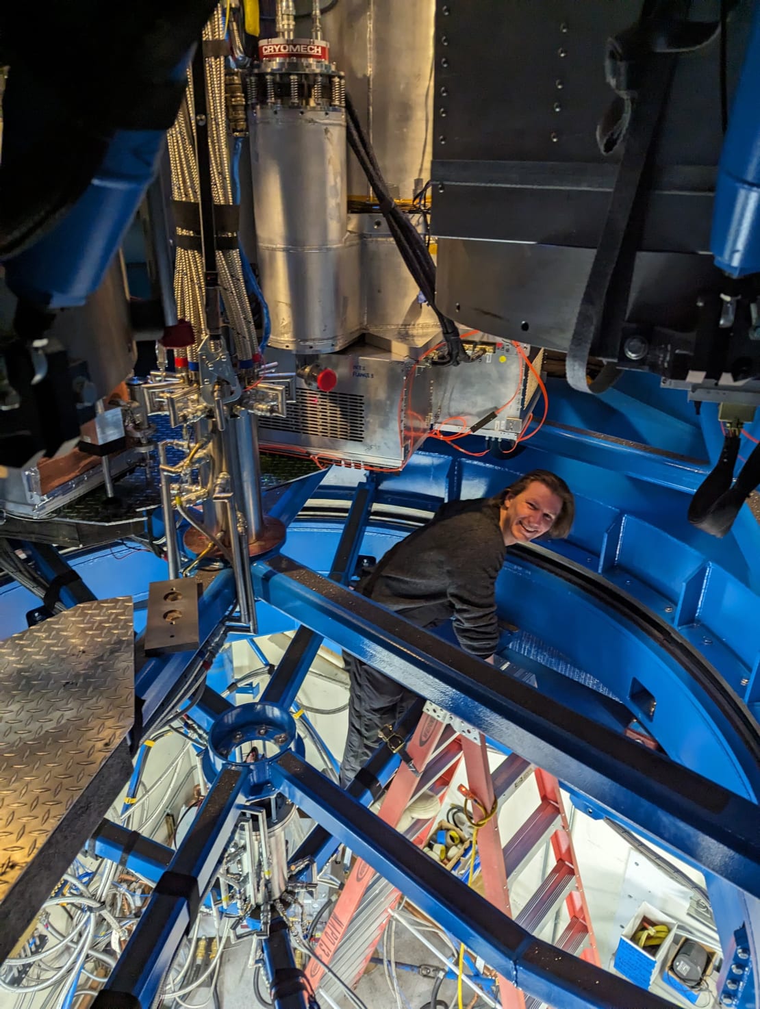 A smiling winterover seen climbing a ladder as they emerge through an opening into the BICEP telescope.