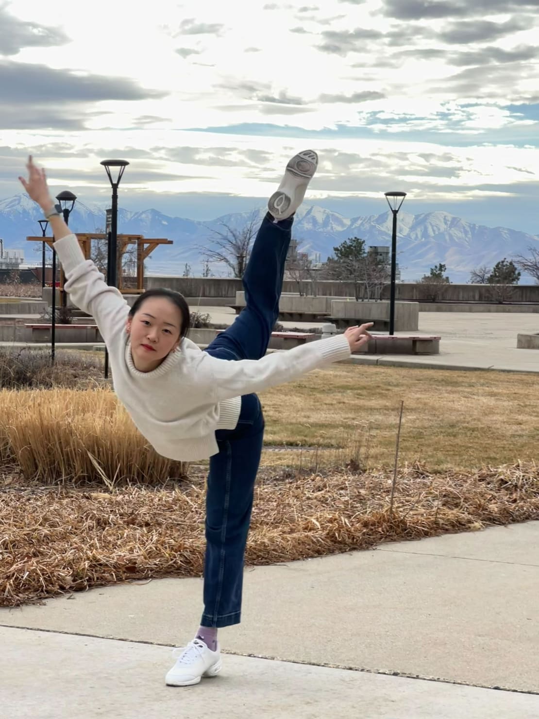A woman wearing a white sweater and jeans standing on one leg.