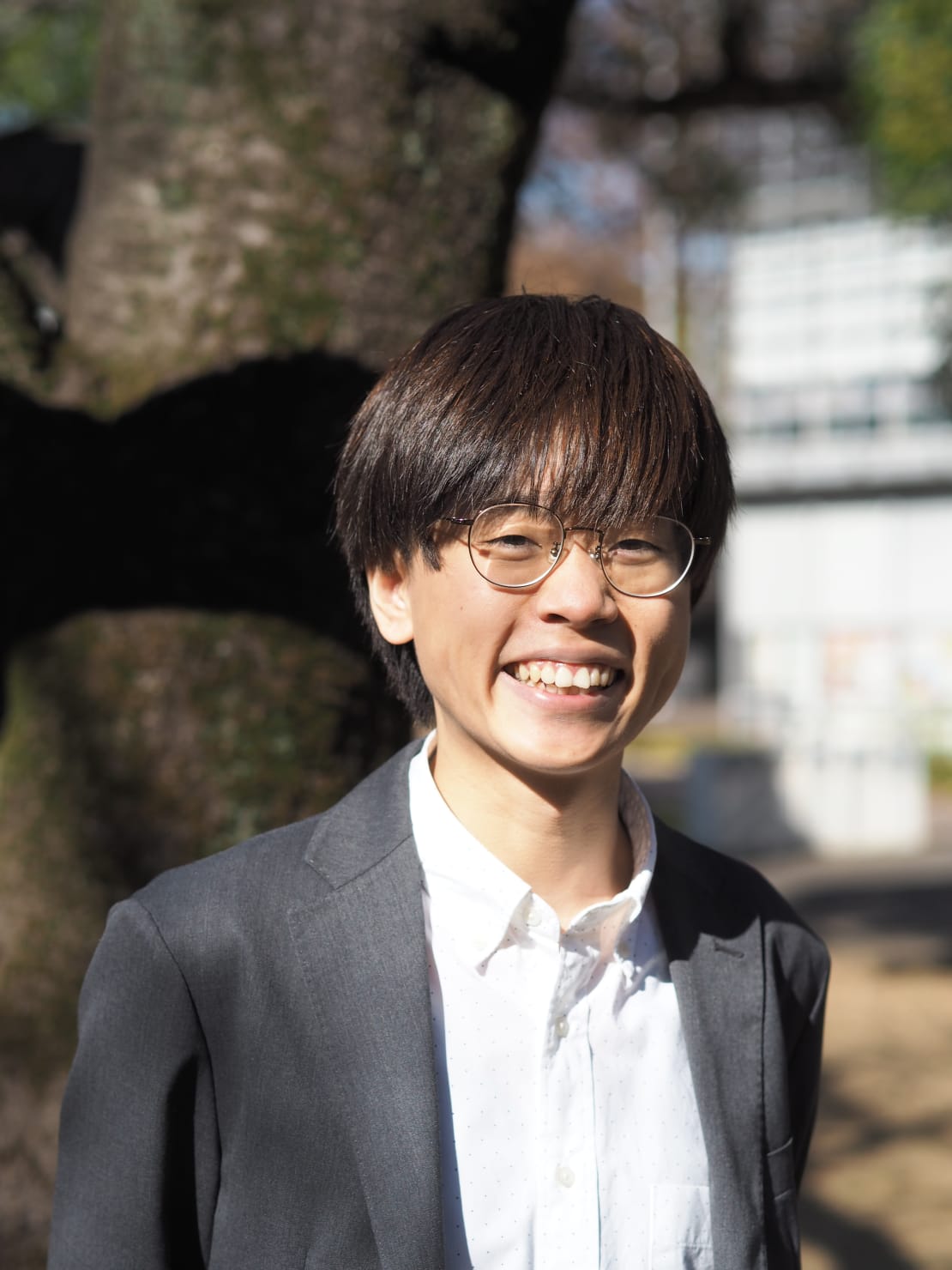 A headshot of a man with glasses in front of a tree.