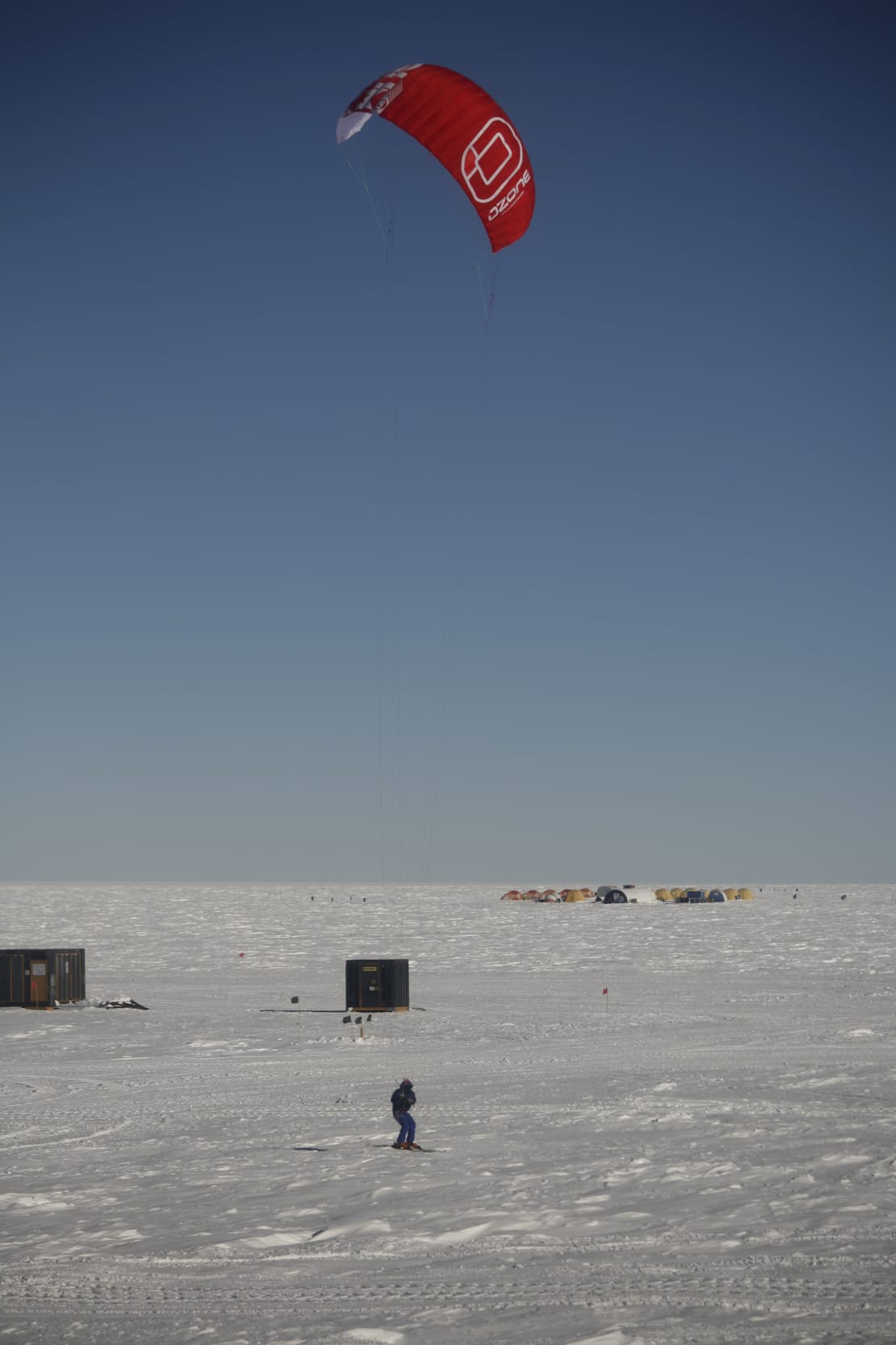 Person out trying to kite-ski at the South Pole, with kite high above then in clear sky.