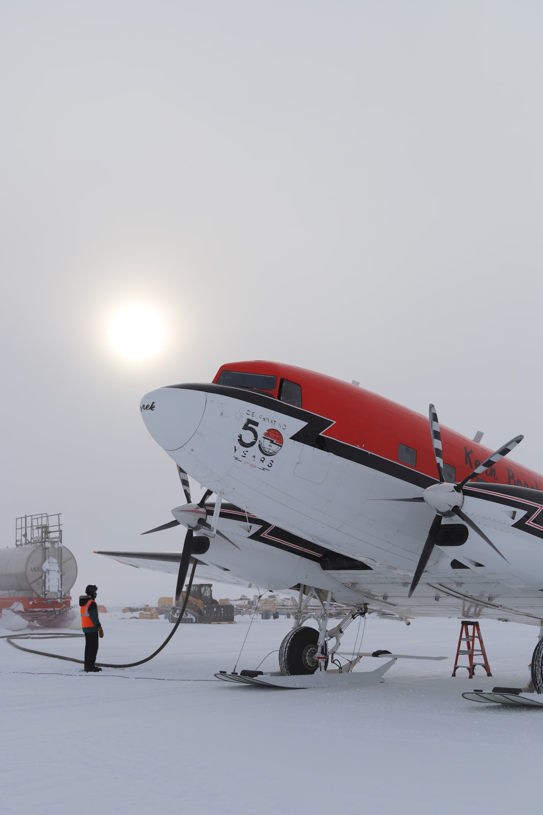 Basler aircraft while being refueled, with overhead un in hazy sky.