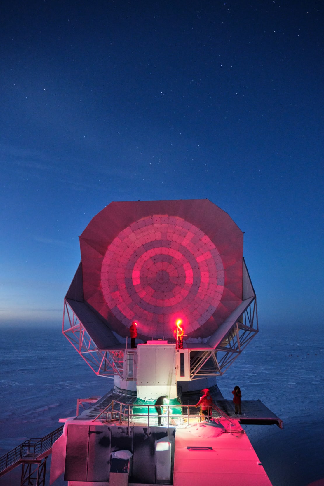 Pink lights lighting up the South Pole Telescope with darkening blue sky at end of sunset.