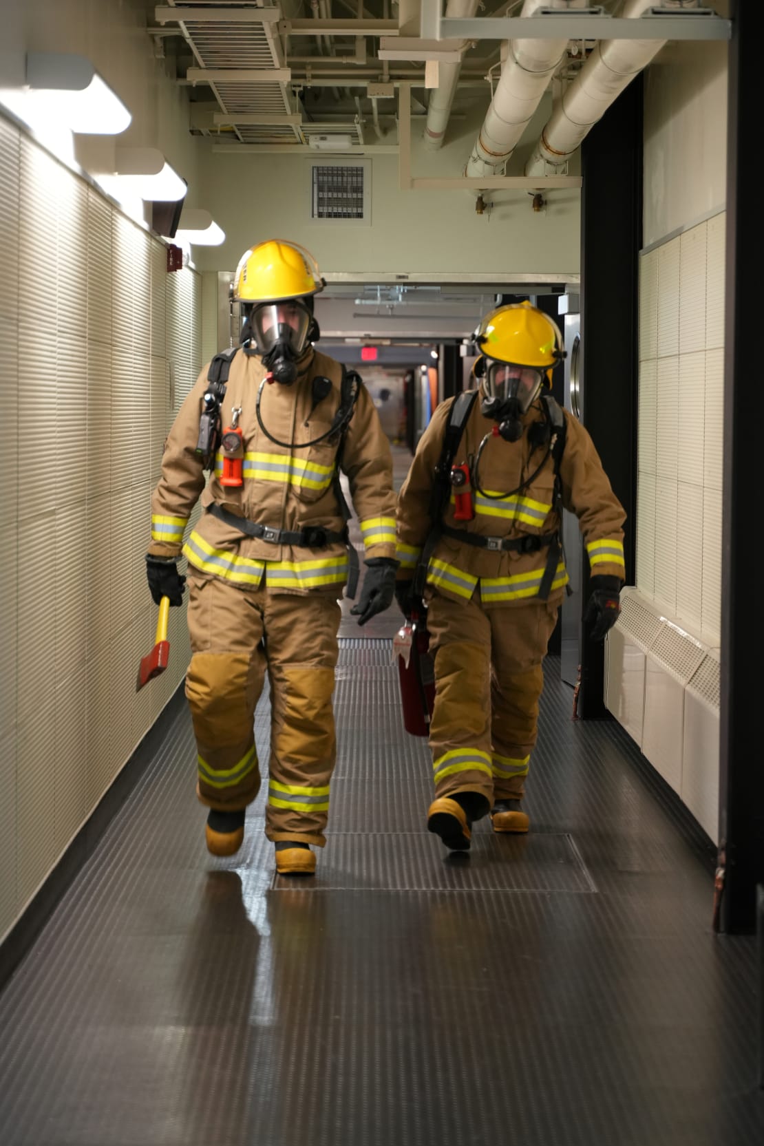 Two winterovers in full firefighting gear walking in station hallway toward the camera.