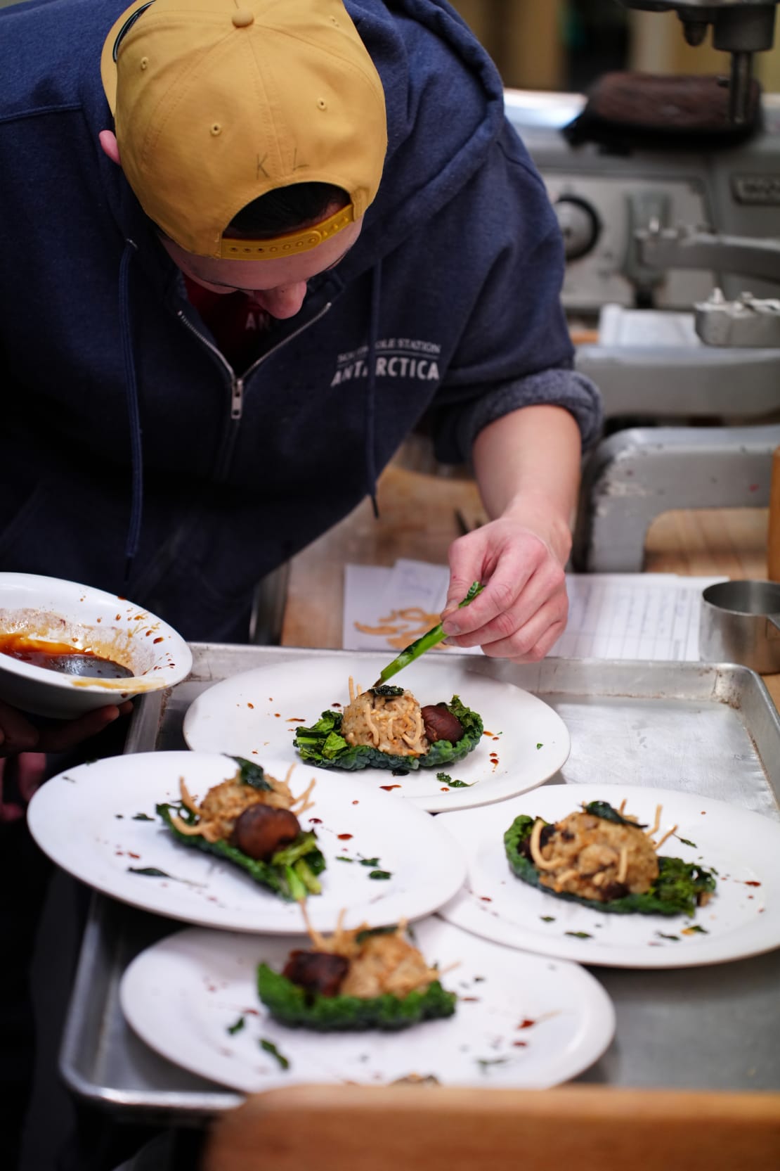 Person bent over, putting finishing touches on plated food.