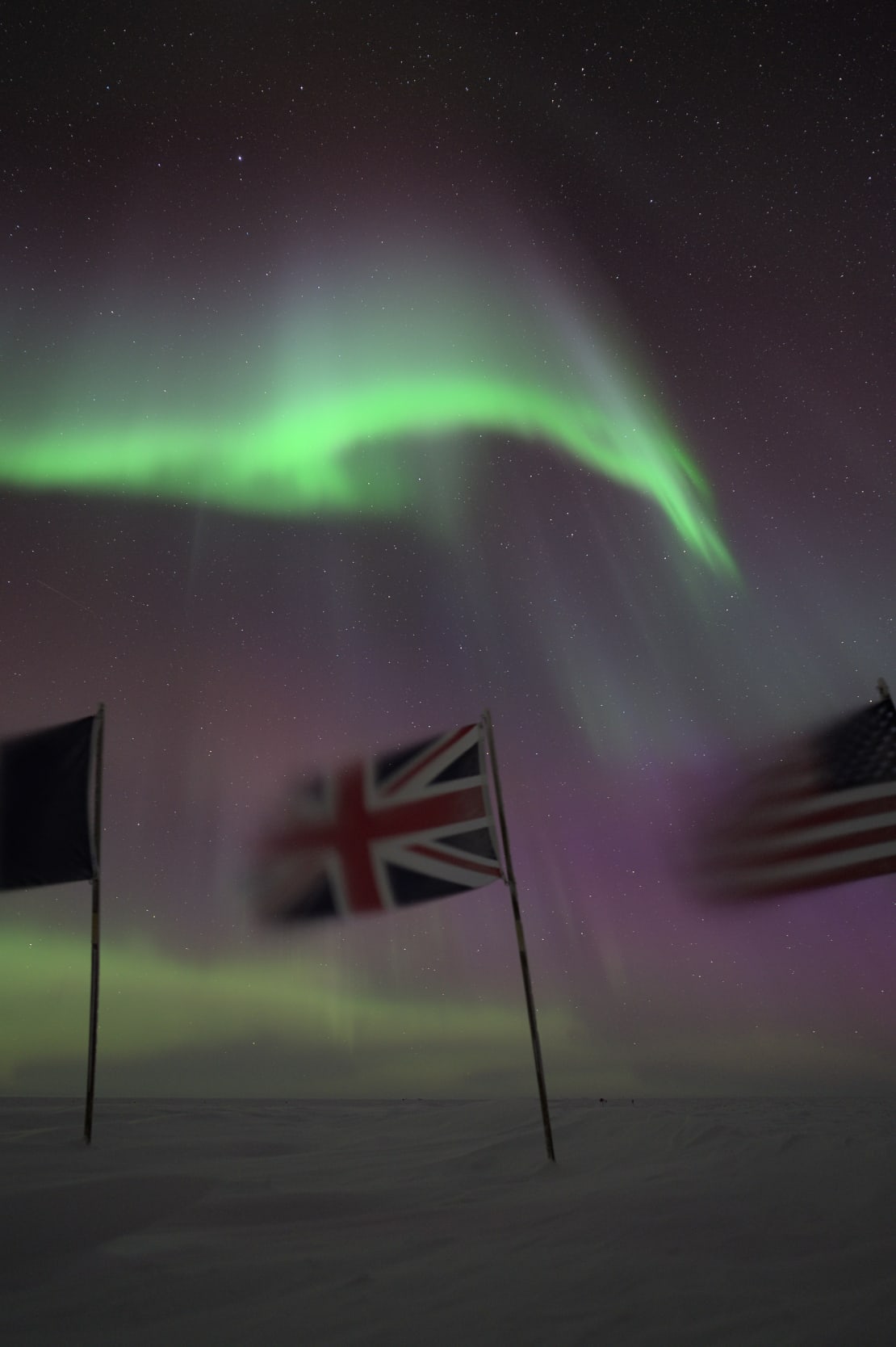Bright green auroras swirling above some of the flags at the ceremonial Pole, flapping in the wind.
