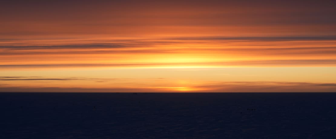 Streaks of horizontal cloudes against sunset sky of yellows and oranges.