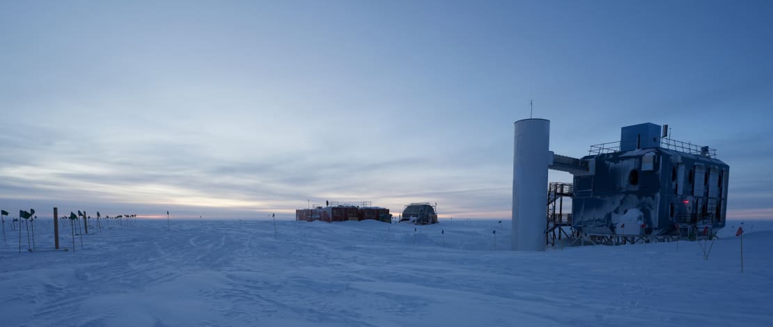 Somewhat cloudy but blue sky at South Pole twilight, IceCube Lab to the right in foreground.
