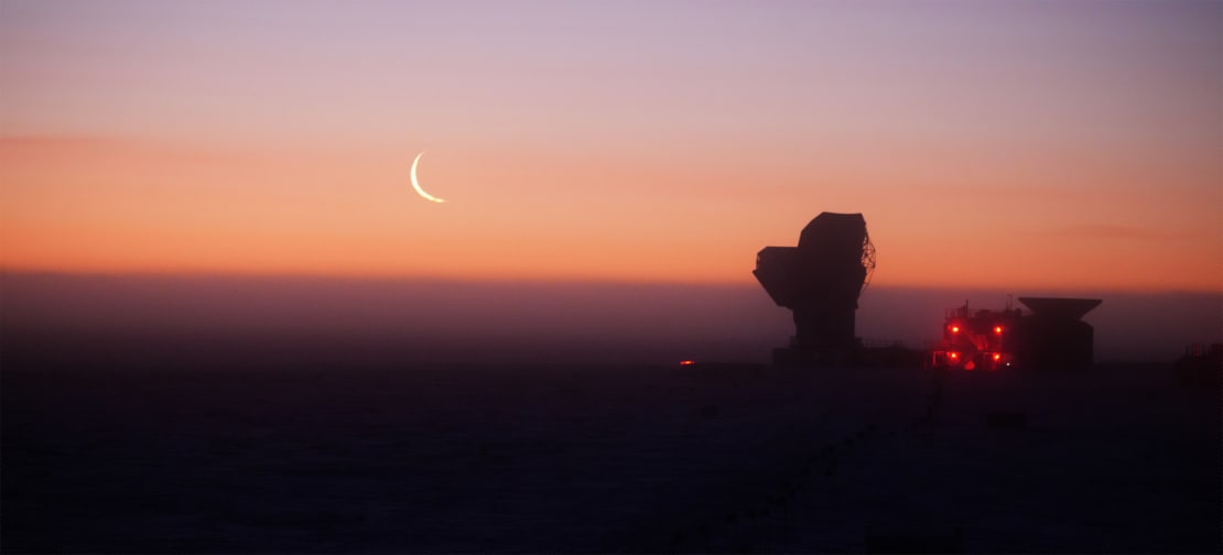 Crescent moon in orange sky, with South Pole Telescope in shadow off to right.