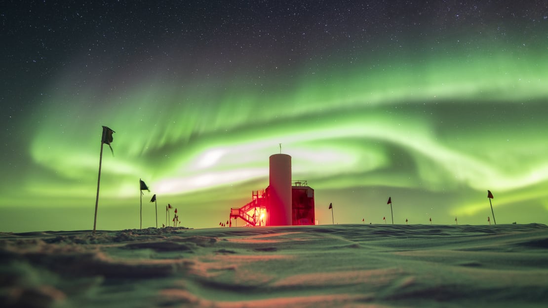 Side view of IceCube Lab with sky full of swirling green auroras.