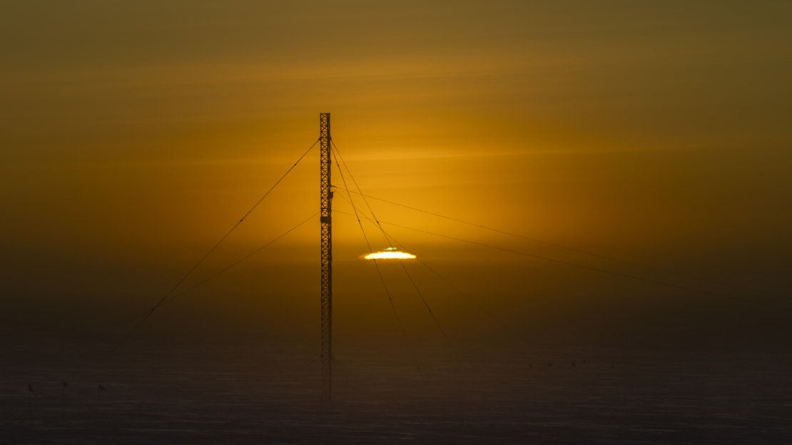 Sun rising at the South Pole, just at horizon with green flash visible, communications tower in foreground.