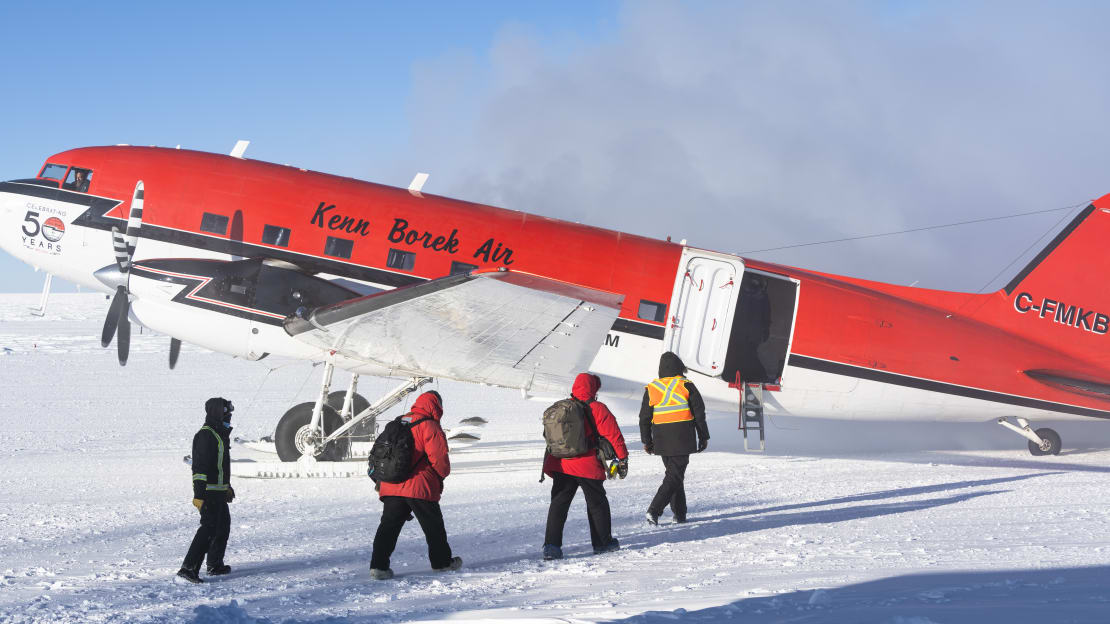 Two winterovers in red parkas approaching an airplane on the ground for departure.