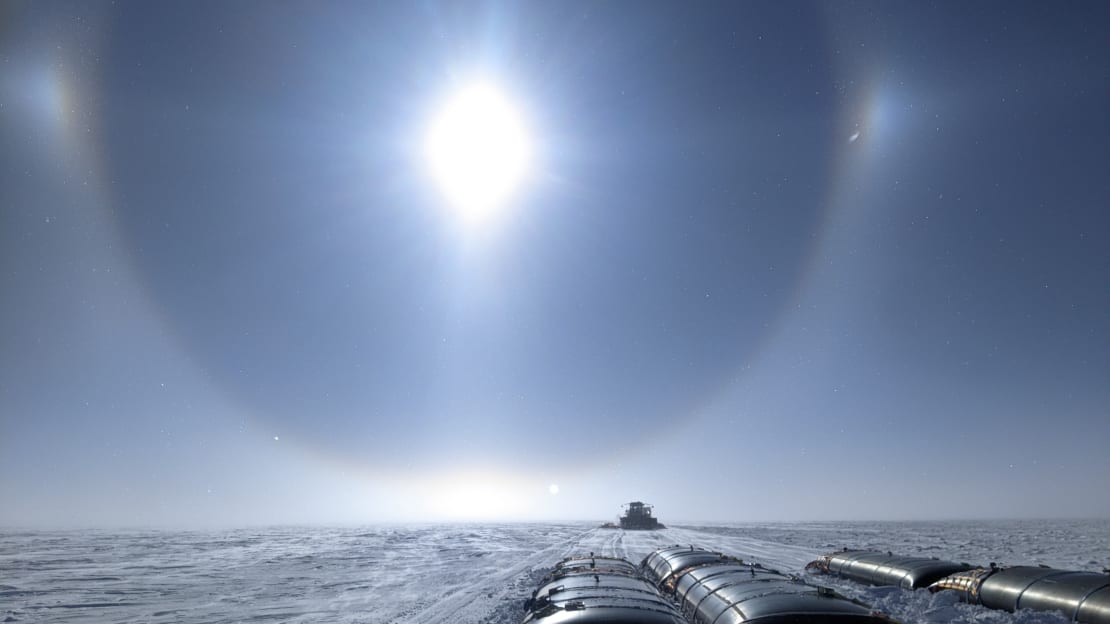 Sun halo filling the sky above snow tractor traverse hauling fuel across the ice.