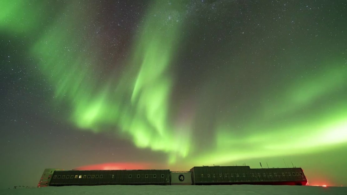 Bright green auroras seemingly emanating upward from the top of the South Pole station.