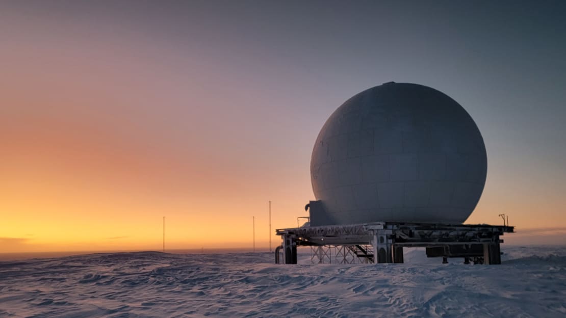 Orange sunlight on horizon at the South Pole, with satellite dome in foreground.