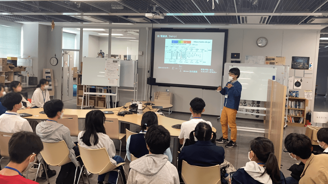 A person gives a lecture in front of a group of students sitting in a lab