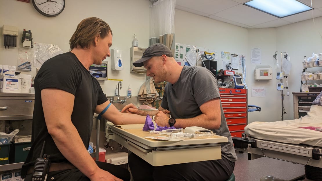 Two winterovers at the South Pole practicing IV insertion in an urgent care room.