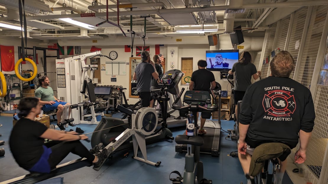 People using gym equipment that is all arranged to view a TV screen showing Star Wars.