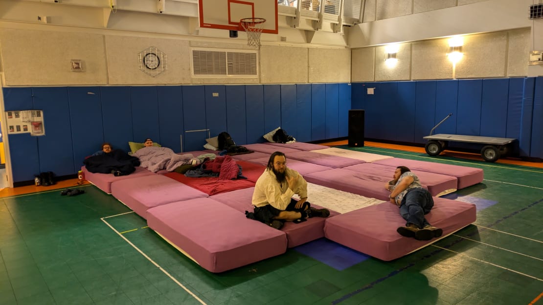 Lots of single mattresses pushed together to form one big bed on the gymnasium floor.