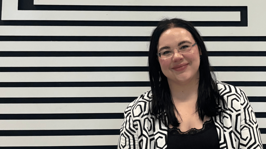 A woman with black hair and glasses posing in front of black and white art.
