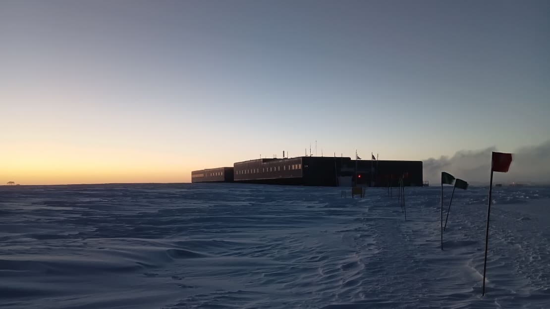 View of the South Pole station at twilight, with some yellow light still lingering on the horizon.