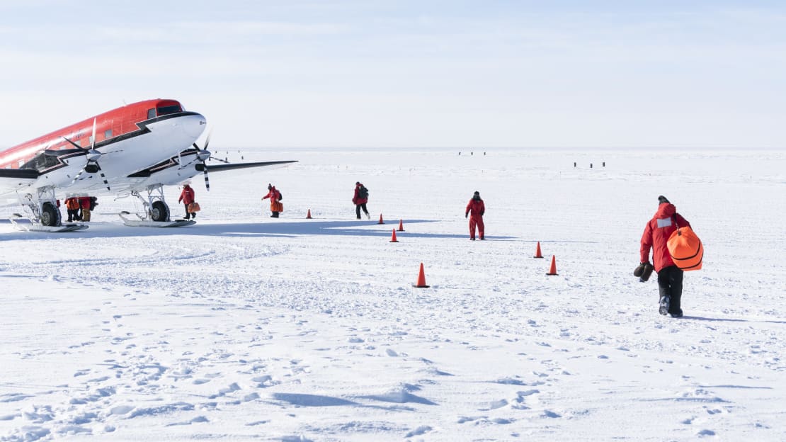 Several people in red parkas from behind making their way toward a plane waiting on the ice.