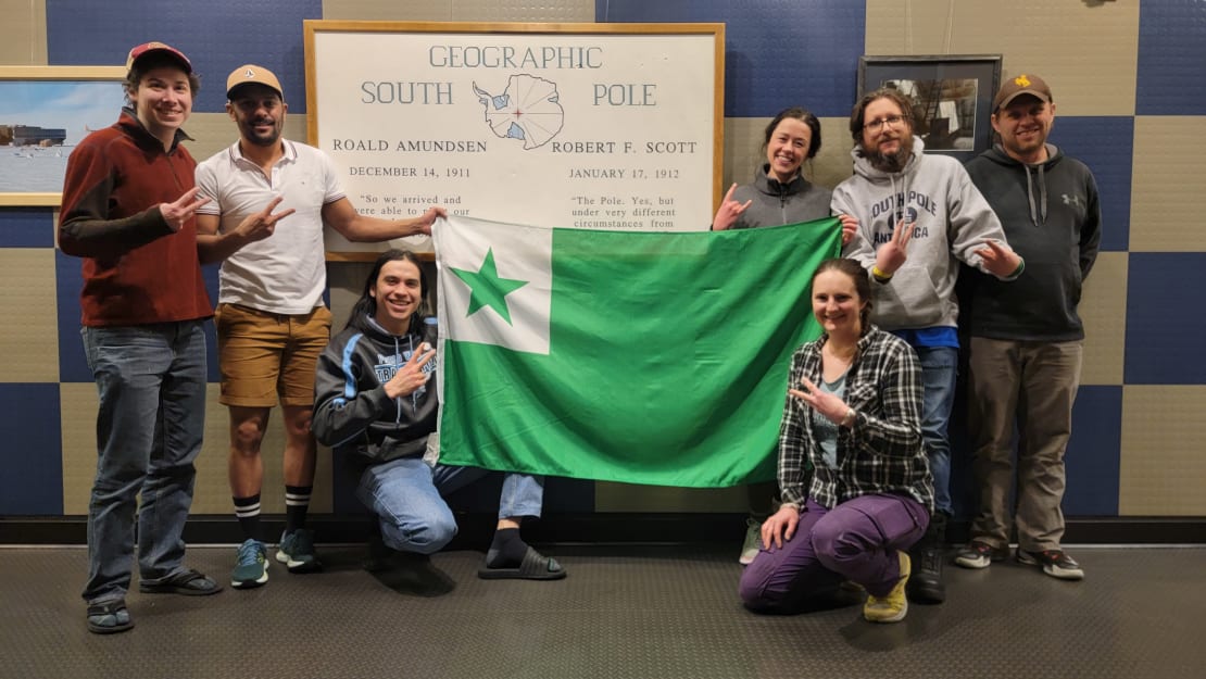 Group photo of South Pole Esperanto club holding up an Esperanto flag.