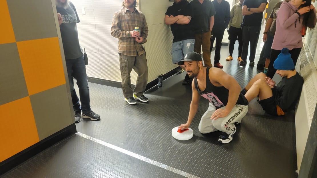 Person crouched down in hallway with curling rock, bystanders around.