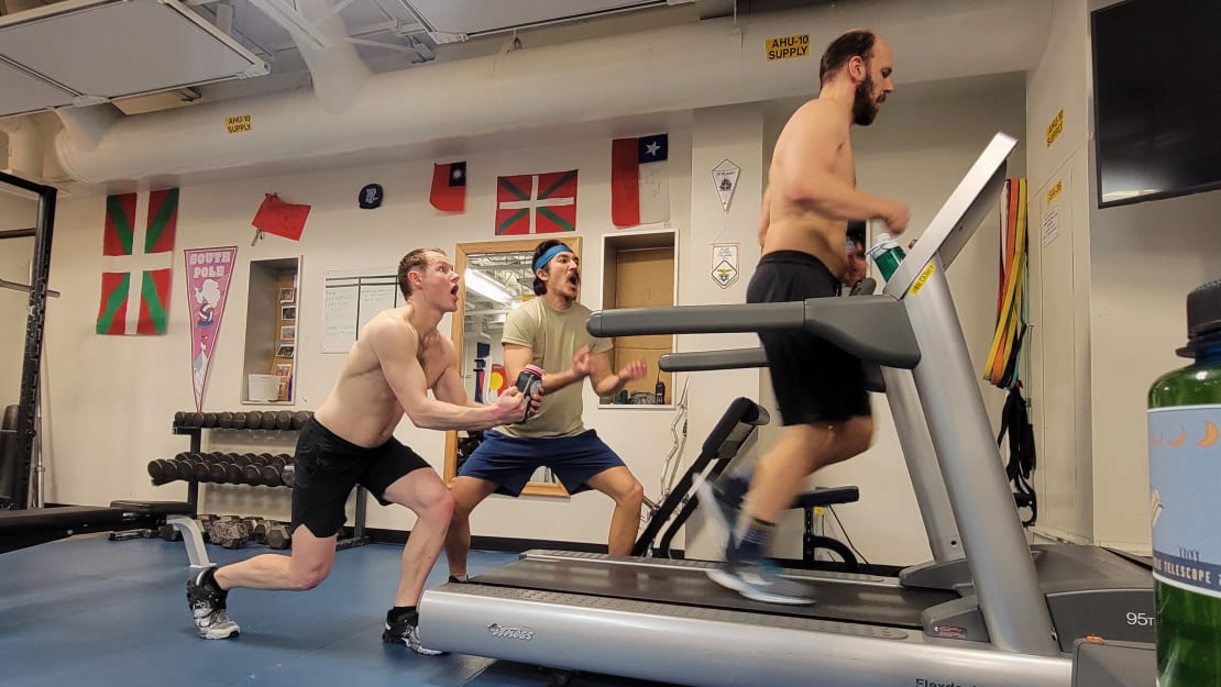 Person running on treadmill, with two behind cheering him on.