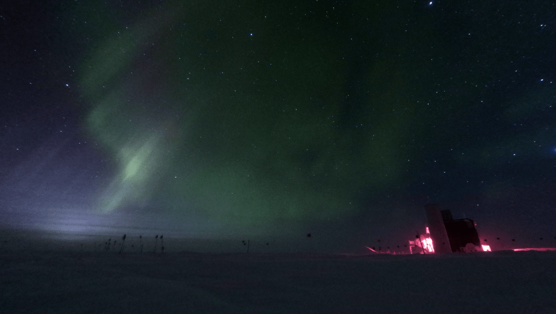 Dark sky with a bit of lingering moonlight along horizon and some faint green auroras.