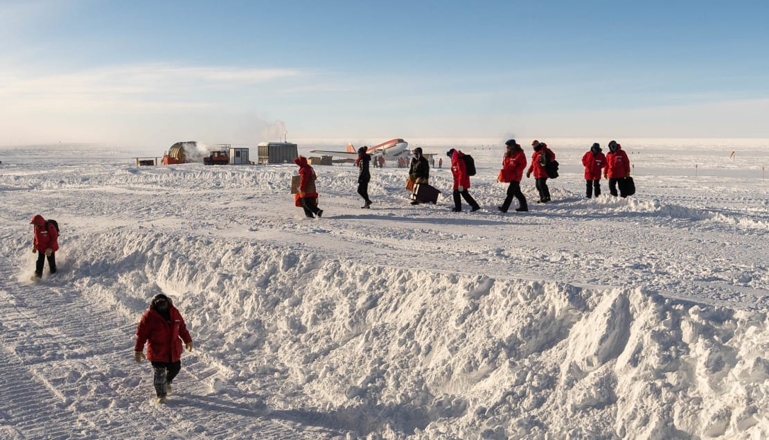 New arrivals to South Pole in red parkas walking on ski way after getting off plane.